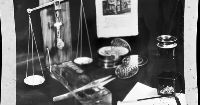 A balance, a loupe and written records laid out together on a bench.